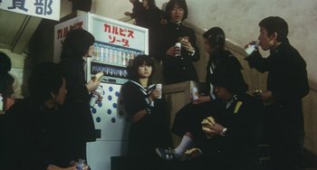 Movie still from “School in the Crosshairs” (1981), directed by Nobuhiko Ôbayashi – A group of people sitting in front of a vending machine; Medium shot, Low angle