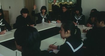Movie still from “School in the Crosshairs” (1981), directed by Nobuhiko Ôbayashi – A group of people sitting around a table; Medium shot, High angle