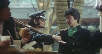 Movie still from “School in the Crosshairs” (1981), directed by Nobuhiko Ôbayashi – A man in black jacket and a man in green jacket; Medium shot, Over the shoulder angle