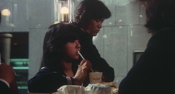 Movie still from “School in the Crosshairs” (1981), directed by Nobuhiko Ôbayashi – A couple of people sitting at a table eating food; Medium shot, Over the shoulder angle