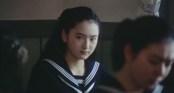 Movie still from “School in the Crosshairs” (1981), directed by Nobuhiko Ôbayashi – A young woman in a sailor's uniform looks into the camera; Close Up shot, Over the shoulder angle