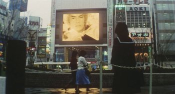 Movie still from “School in the Crosshairs” (1981), directed by Nobuhiko Ôbayashi – Two women walking in front of a large screen; Extreme Wide shot, Low angle