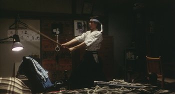 Movie still from “School in the Crosshairs” (1981), directed by Nobuhiko Ôbayashi – A man holding a baseball bat in a room; Wide shot, High angle