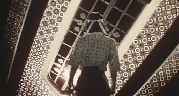 Movie still from “School in the Crosshairs” (1981), directed by Nobuhiko Ôbayashi – A woman in a floral print shirt is walking up a flight of stairs; Medium shot, Low angle