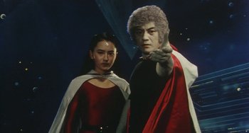 Movie still from “School in the Crosshairs” (1981), directed by Nobuhiko Ôbayashi – A man and a woman dressed in red and white standing next to each other in front of a dark background; Medium shot, Low angle
