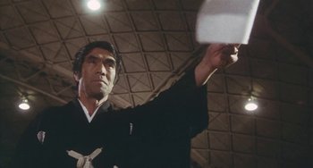 Movie still from “School in the Crosshairs” (1981), directed by Nobuhiko Ôbayashi – A man in a black kimono is throwing a frisbee; Medium shot, Low angle