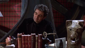 Movie still from “Scooby-Doo” (2002), directed by Raja Gosnell – A man sitting in front of a row of books on top of a table; Medium shot, High angle