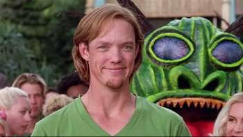 Movie still from “Scooby-Doo” (2002), directed by Raja Gosnell – A man with long blonde hair wearing a green t - shirt; Close Up shot, Over the shoulder angle