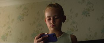 Movie still from “Scrapper” (2023), directed by Charlotte Regan – A young girl looking at her cell phone; Close Up shot, Low angle