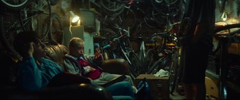 Movie still from “Scrapper” (2023), directed by Charlotte Regan – A young boy sitting in a chair in front of a bunch of bikes; Wide shot, High angle