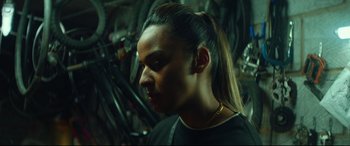 Movie still from “Scrapper” (2023), directed by Charlotte Regan – A man with long black hair is looking to his left; Close Up shot, Over the shoulder angle