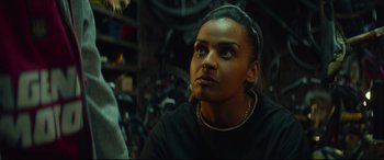 Movie still from “Scrapper” (2023), directed by Charlotte Regan – A woman looking up while sitting in a garage; Close Up shot, Over the shoulder angle