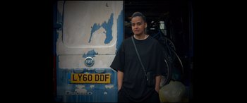 Movie still from “Scrapper” (2023), directed by Charlotte Regan – A man standing in front of an old bus; Medium shot, Low angle