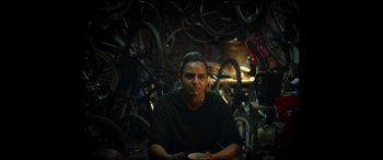 Movie still from “Scrapper” (2023), directed by Charlotte Regan – A person sitting in a room with many bicycles; Medium shot, Over the shoulder angle