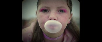 Movie still from “Scrapper” (2023), directed by Charlotte Regan – A young girl is chewing on a bubble gum; Close Up shot, Over the shoulder angle