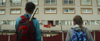 Movie still from “Scrapper” (2023), directed by Charlotte Regan – A man hanging clothes on a clothes line outside of a building; Wide shot, Over the shoulder angle