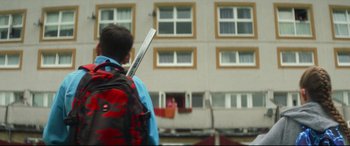 Movie still from “Scrapper” (2023), directed by Charlotte Regan – A boy with a backpack and a stick in his hand; Medium shot, Low angle