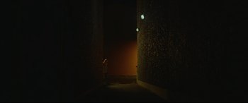 Movie still from “Scrapper” (2023), directed by Charlotte Regan – A person standing in a dark room next to a wall; Extreme Wide shot, Low angle