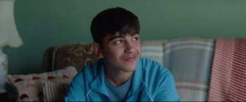 Movie still from “Scrapper” (2023), directed by Charlotte Regan – A young man in a blue shirt is smiling; Close Up shot, Over the shoulder angle