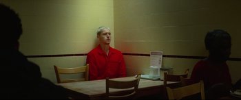 Movie still from “Scrapper” (2023), directed by Charlotte Regan – A man sitting at a table in front of a wall; Medium shot, Low angle