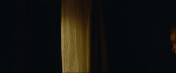 Movie still from “Scrapper” (2023), directed by Charlotte Regan – A dark room with a curtain and a light; Medium shot, Low angle