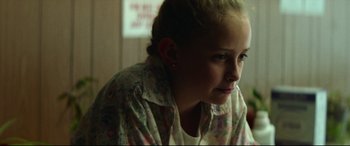 Movie still from “Scrapper” (2023), directed by Charlotte Regan – A young girl sitting in front of a window looking sad; Close Up shot, Over the shoulder angle