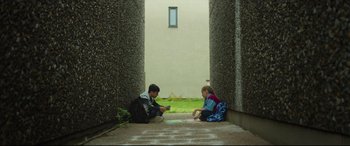 Movie still from “Scrapper” (2023), directed by Charlotte Regan – Two children sitting on the steps of a building; Wide shot, Low angle