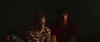 Movie still from “Scrapper” (2023), directed by Charlotte Regan – Two young people sitting in a dark room; Medium shot, High angle