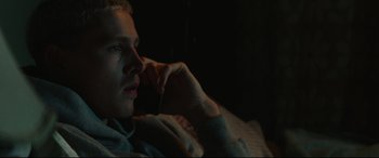 Movie still from “Scrapper” (2023), directed by Charlotte Regan – A man sitting in a dark room with his hand under his chin; Close Up shot, Low angle