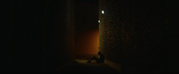 Movie still from “Scrapper” (2023), directed by Charlotte Regan – A person sitting on the ground in a dark room; Extreme Wide shot, Low angle