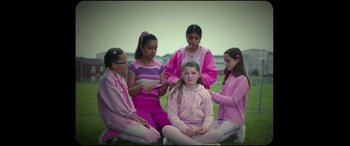 Movie still from “Scrapper” (2023), directed by Charlotte Regan – A group of young girls sitting on the grass; Medium shot, Over the shoulder angle