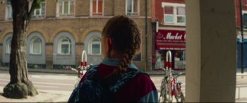 Movie still from “Scrapper” (2023), directed by Charlotte Regan – A woman with a braid standing in front of a building; Close Up shot, Low angle