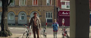 Movie still from “Scrapper” (2023), directed by Charlotte Regan – A man and a woman standing in front of a row of bicycles; Wide shot, Low angle