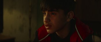 Movie still from “Scrapper” (2023), directed by Charlotte Regan – A young man wearing a red and black jacket; Close Up shot, Over the shoulder angle