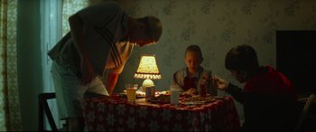 Movie still from “Scrapper” (2023), directed by Charlotte Regan – A man and a child are sitting at a table; Medium shot, High angle