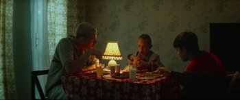 Movie still from “Scrapper” (2023), directed by Charlotte Regan – A man and a boy sitting at a table with a lit candle; Medium shot, High angle
