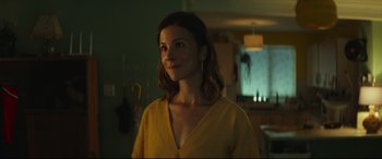 Movie still from “Scrapper” (2023), directed by Charlotte Regan – A woman standing in a room with a smile on her face; Close Up shot, Over the shoulder angle