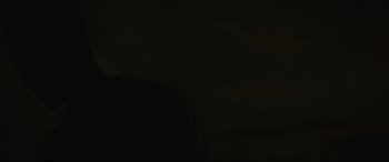 Movie still from “Scrapper” (2023), directed by Charlotte Regan – A person standing in a dark room with dark clouds in the background; Close Up shot, Low angle