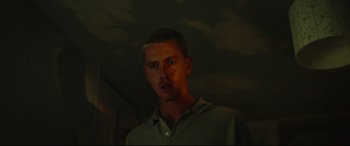 Movie still from “Scrapper” (2023), directed by Charlotte Regan – A man in a dark room looking at the camera; Close Up shot, Low angle