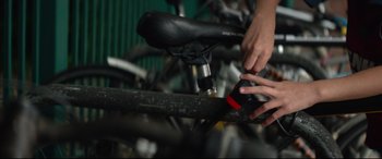 Movie still from “Scrapper” (2023), directed by Charlotte Regan – A person using a cell phone on a bicycle; Extreme Close Up shot, High angle