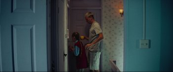 Movie still from “Scrapper” (2023), directed by Charlotte Regan – An older man and a young girl are standing in front of a door; Medium shot, High angle