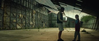 Movie still from “Scrapper” (2023), directed by Charlotte Regan – A man standing next to a wall in an abandoned building; Extreme Wide shot, Low angle