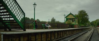 Movie still from “Scrapper” (2023), directed by Charlotte Regan – A couple of people sitting on top of a wooden bench; Extreme Wide shot, Low angle