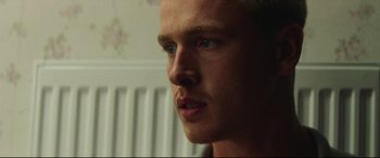 Movie still from “Scrapper” (2023), directed by Charlotte Regan – A man's face in front of a radiator; Close Up shot, Low angle