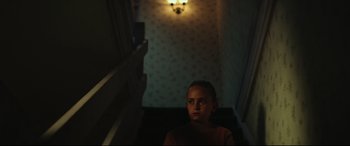 Movie still from “Scrapper” (2023), directed by Charlotte Regan – A young girl standing in a dark hallway; Medium shot, Low angle