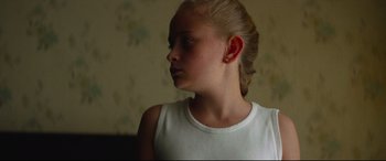 Movie still from “Scrapper” (2023), directed by Charlotte Regan – A young girl with blonde hair wearing a white tank top; Close Up shot, Low angle