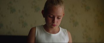 Movie still from “Scrapper” (2023), directed by Charlotte Regan – A young girl in a white tank top looking down at her face; Close Up shot, High angle
