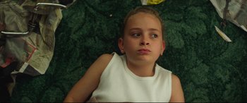Movie still from “Scrapper” (2023), directed by Charlotte Regan – A young girl is laying on the ground looking at the camera; Close Up shot, High angle