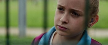 Movie still from “Scrapper” (2023), directed by Charlotte Regan – A young girl with a blue and pink shirt; Close Up shot, Over the shoulder angle