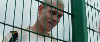 Movie still from “Scrapper” (2023), directed by Charlotte Regan – A person behind a green fence; Close Up shot, High angle